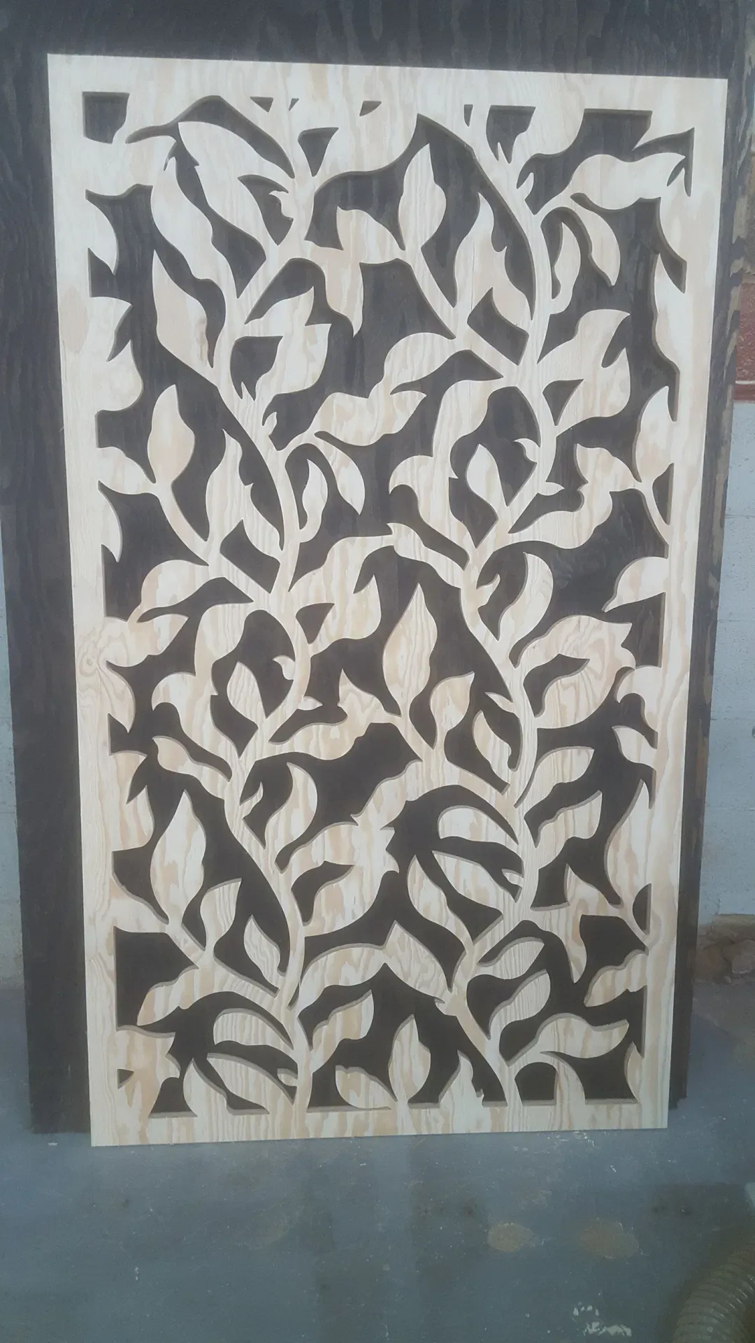 A custom laser-cut wood panel featuring an intricate, flowing botanical leaf pattern. The natural wood grain of the light-colored surface contrasts sharply against the dark, negative spaces of the cutout design. This decorative piece demonstrates our precision craftsmanship, serving as an elegant solution for room dividers, wall art, or architectural screens that require a sophisticated, organic aesthetic.