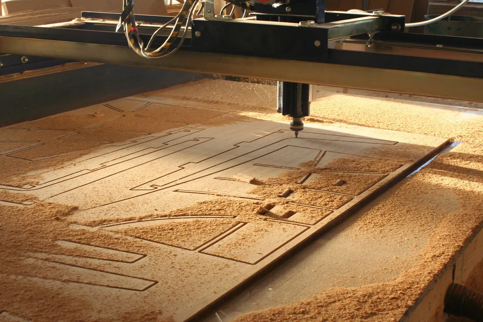 This image captures our CNC router in action, precisely cutting intricate component shapes from a large sheet of plywood. The photo highlights the automation and accuracy we utilize in our workshop to create complex furniture parts with minimal waste. The workspace is covered in sawdust, showcasing an active project mid-production. This illustrates our commitment to combining modern technology with traditional craftsmanship to ensure every piece we manufacture meets exact specifications for our clients' custom furniture and cabinetry orders.
