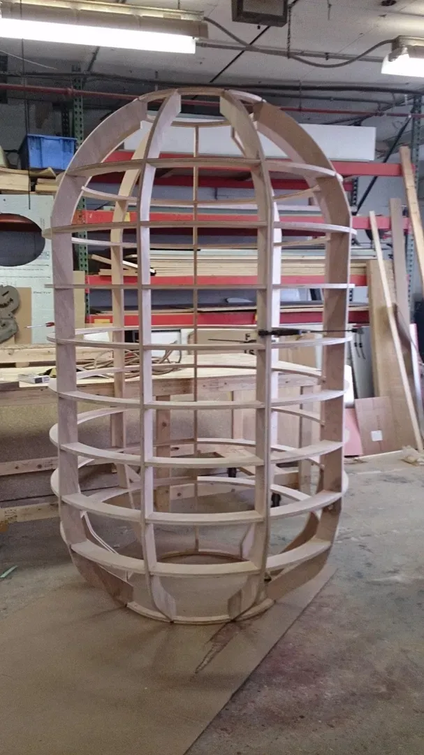 This image showcases the initial skeletal structure of a custom wooden installation, currently under construction in our workshop. The frame, nicknamed "xWmw" for tracking, features precision-cut interlocking plywood ribs forming a large, egg-shaped pod. This sturdy framework represents the foundational stage of our fabrication process before exterior finishes or lighting are applied. It highlights the structural integrity and craft quality we bring to our bespoke design and build projects.